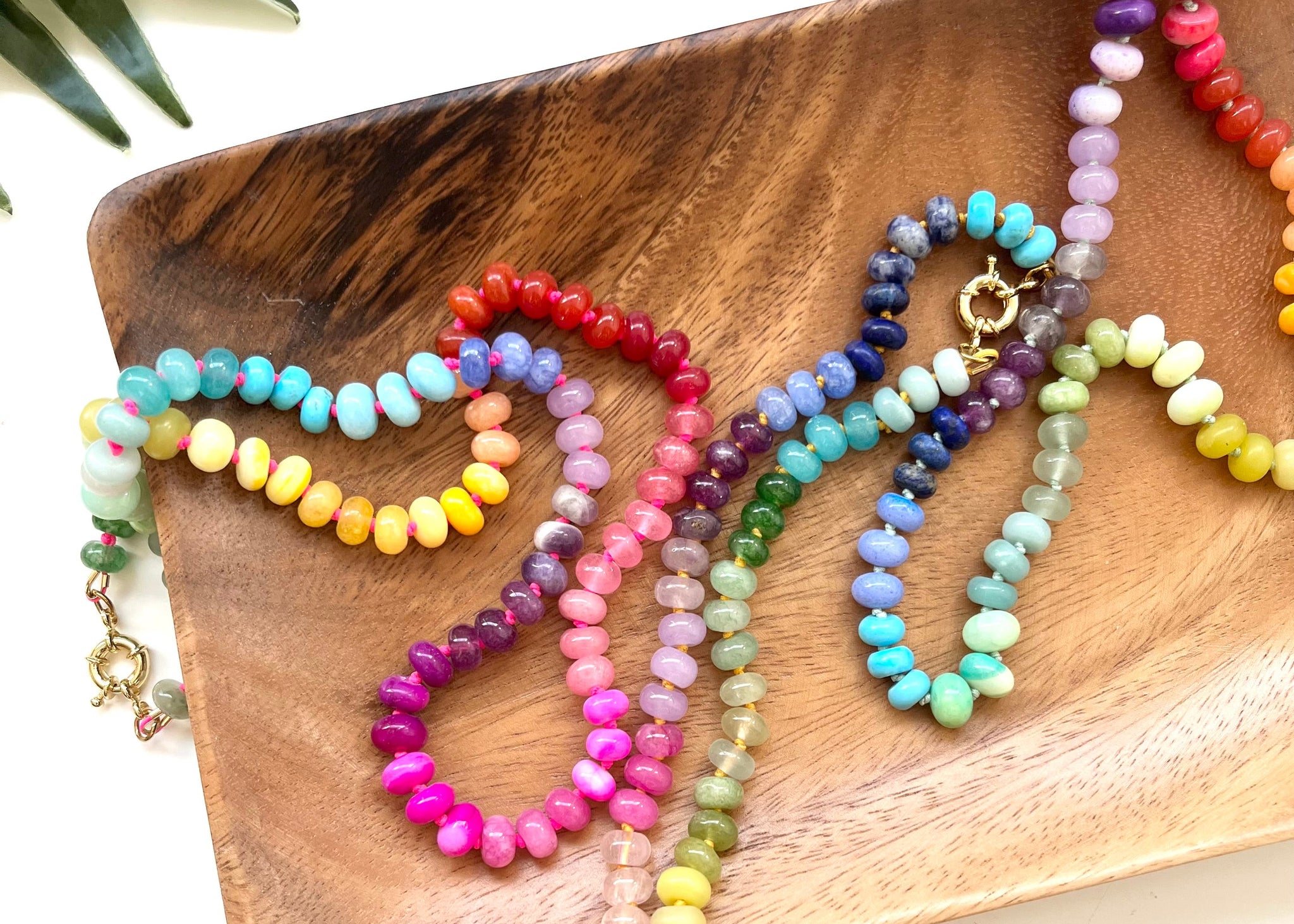 Colorful beaded necklaces on a wooden surface with a leafy background